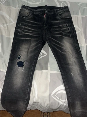 Svarta slitna jeans med hål - Säljer ett par svarta jeans med slitningar och hål på vänster ben. Jeansen har en tvättad look med ljusare partier och klassisk femficksmodell. Passar dig som gillar en edgy och avslappnad stil.