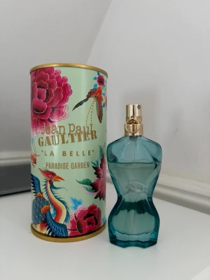 Jean Paul Gaultier La Belle Paradise Garden - Unik parfymflaska i turkost glas formad som en kvinnokropp, med guldfärgad spraykork. Kommer i en färgglad cylinderförpackning med blommor och fåglar. Doften heter 'La Belle Paradise Garden' och är en riktig statement-parfym.