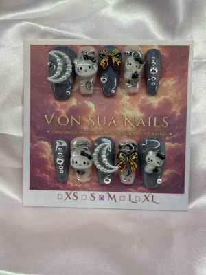 MoonKitty (M);Medium Coffin - Unika handgjorda press-on naglar med svart och silverglittrig bas, dekorerade med 3D-HK, månar, stjärnor och färgglada rosetter. Mix av matta och blanka detaljer samt små pärlor och stenar för extra effekt. Perfekt för dig som vill ha något gulligt och kreativt på naglarna.M: 16 mm, 12 mm, 12,5 mm, 11,5 mm, 10 mm