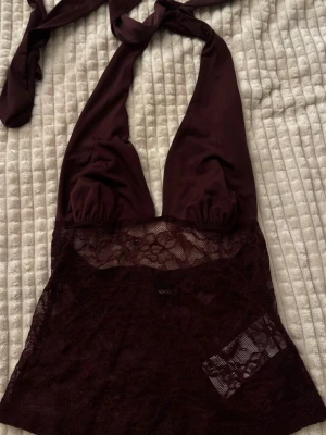 Laced Halter Top - Vinröd halternecktopp med djup urringning. Överdelen är i mjuk, slät textil och nedre delen i transparent med spets. Öppen rygg och har  knytband i nacken för justerbar passform. 