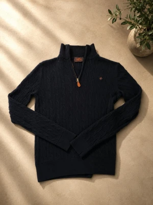 Mörkblå kabelstickad tröja halvzip - Mörkblå Morris tröja med halv dragkedja och broderad detalj på bröstet. Tröjan har långa ärmar och ribbade muddar. Perfekt för lager på lager och ger en klassisk look. Skriv gärna för frågor! Har krympt lite i tvätten så är kanske mer som en xs.