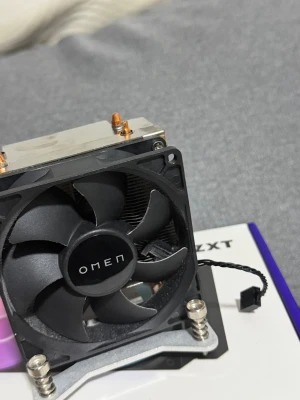 OMEN CPU-kylare med fläkt - Säljer en svart OMEN CPU-kylare med fläkt och kylfläns i metall. Fläkten har fem blad och ansluts med en 4-pin kontakt. Kylflänsen är i aluminium med kopparrör för effektiv värmeavledning. Perfekt för gamingdatorer eller uppgraderingar.