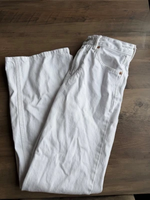 Vita raka jeans D92 - Säljer ett par vita jeans från D92 med rak passform och klassisk femficksdesign. Jeansen har en patch med D92-logga bak i midjan och är tillverkade i ett kraftigare bomullstyg. Perfekta för dig som vill ha en clean och stilren look.