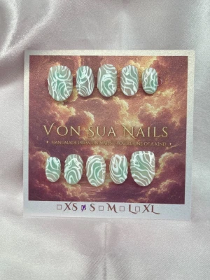 Fern (S);ExtraShortOval  - Snygga handgjorda press-on naglar i en mjuk turkos blush färg med vitt handmålade mönster . Naglarna har en oval form och är perfekta för dig som vill ha en unik och trendig look. Materialet är tåligt och lätt att applicera.