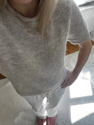 Ljusgrå stickad t-shirt - Kortärmad stickad t-shirt i ljusgrått med rund hals. Tröjan har en mjuk och fluffig känsla, perfekt för lager på lager. Passar till både jeans och kjol för en avslappnad look.