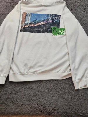 Vit t-shirt med grön graffiti-tryck - Säljer en vit t-shirt från DIVINE med ett grönt graffiti-inspirerat tryck på bröstet. T-shirten är i mjuk bomull och har klassisk passform med korta ärmar. Perfekt för dig som gillar streetwear och vill sticka ut med en cool detalj.