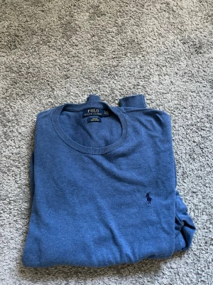 Blå stickad tröja från Polo Ralph Lauren - Snygg blå stickad tröja från Polo Ralph Lauren med rund halsringning och diskret broderad logga på bröstet. Tröjan har en klassisk passform och är perfekt för alla laidback. 