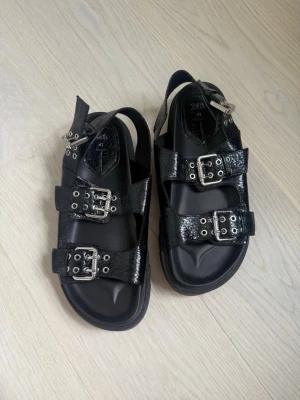 Zara- Nya svarta sandaler med spännen - Snygga svarta sandaler med tre justerbara metallspännen och grov sula. Sandalerna har en glansig finish och coola detaljer i silver.