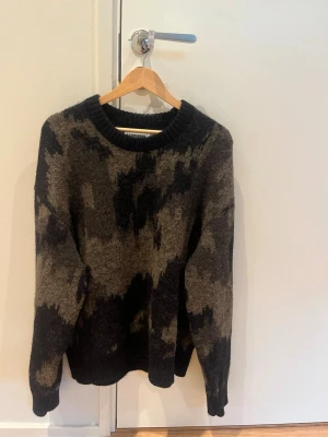 Mörk mönstrad stickad tröja J.Lindeberg - Stickad tröja från J.Lindeberg i mörkgrå och svart färg med abstrakt mönster. Tröjan har rund halsringning med bred ribbstickad kant och långa ärmar. Materialet ser ut att vara ullblandning, perfekt för kyliga dagar. Storlek S men passar även mig som använder M vanligtvis 