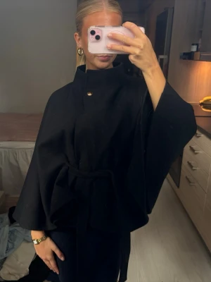 Nelly cape-kappa  - Svart kappa med snöre och guldknapp på kragen, knappt använd, köpt på Nelly för 400kr
