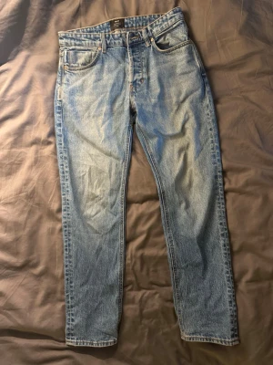 Ljusblå raka jeans med fem fickor - Säljer ett par klassiska ljusblå jeans med rak passform och fem fickor. Jeansen har normal midja, bälteshällor och dragkedjegylf. Perfekta för en avslappnad och stilren look. Materialet är denim i bomull.