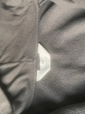 Mörkgrå hoodie från H&M - En enkel och stilren mörkgrå hoodie från H&M. Hoodien har en klassisk huva och är tillverkad i mjukt bomullsmaterial med borstad insida för extra komfort. Perfekt för en avslappnad look och passar till det mesta i garderoben.