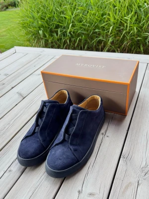 Mörkblå sneakers i mocka från Myrqvist - Sneakers från Myrqvist - Alnö Monochrome. Stilrena mörkblå sneakers i mocka från Myrqvist. Skorna har en låg profil och elastiska band istället för klassiska snören. Insidan är fodrad i ljust läder för extra komfort. Mycket hög kvalitet och bra skick på detta exemplar. Originalkartong medföljer. 