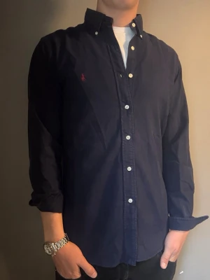 Ralph Lauren skjorta marinblå – M slim fit - Säljer denna stilrena och snygga marinblå Ralph Lauren skjorta. Skjortan är i mycket bra skick och storlek M slim fit. Perfekt för både vardag och mer uppklädda tillfällen. Har du några frågor? Tveka inte att höra av dig. Allt gott från Deluxe Garderoben ⭐️
