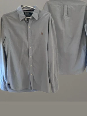  Ralph Lauren skjorta  - Klassisk ljusblå skjorta från Polo Ralph Lauren med button-down krage och broderad logga på bröstet i storlek medium. Skjortan har långa ärmar, knappar framtill och är tillverkad i mjuk bomull. Perfekt till både jeans och chinos. Skriv vid frågor. 