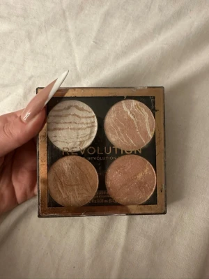 Bronzerpalett med fyra nyanser - Snygg bronzerpalett från Revolution med fyra skimrande nyanser i beige, guld, koppar och champagne. Pudret har en marmorerad finish och kommer i en fyrkantig plastförpackning med genomskinligt lock. Perfekt för att skapa glow och värme i ansiktet.