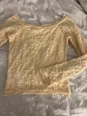 Ljusgul topp med lång ärm - Säljer en ljusgul blus i spets med lång ärm och offshoulder-design. Blusen har fina spetsdetaljer över hela plagget och en feminin, romantisk look. Perfekt för dig som gillar unika toppar med mycket detaljer.