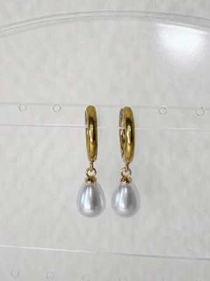 Guldiga örhängen med droppformade pärlor - Snygga örhängen i guldfärgad metall med droppformade vita pärlor som hänger ner. Perfekta för att lyfta vilken outfit som helst. Örhängena har en enkel ringformad bas och pärlorna ger en elegant touch.