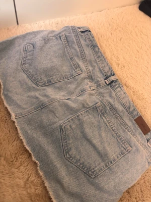 Ljusblå jeanskjol från Subdued - Säljer en ljusblå jeanskjol i klassisk denim med rå, fransig kant nedtill. Kjolen har femficksmodell, bälteshällor och är från subdued