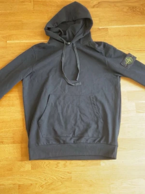 Svart hoodie  - Säljer en svart hoodie med klassisk patch på vänster ärm. Hoodien har stor huva med dragsko och en rymlig magficka framtill. Tillverkad i mjukt bomullsmaterial och har ribbade muddar vid ärmslut och nederkant.