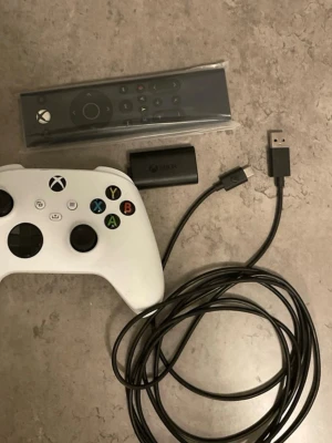Vit Xbox-handkontroll med tillbehör(kvitto)finns  - Säljer en vit Xbox-handkontroll med matchande fjärrkontroll, laddningsbart batteripack och lång USB-kabel. Handkontrollen har klassisk Xbox-design med svarta och färgade knappar. Perfekt för gaming på konsol eller PC.