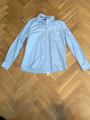 Ljusblå skjorta från Dressmann - Klassisk ljusblå skjorta från Dressmann i bomull i storlek L. Skjortan har lång ärm, bröstficka och knappar framtill. Perfekt till jeans eller chinos för en clean look. Skicka prisförslag🙌