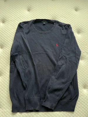 Polo Ralph Lauren finstickad långärmad tröja mörkblå - Finstickad tröja från polo Ralph lauren i storlek XL. Broderade loggan på bröstet är rött/mörkrosa. Tröjan är i fint skick men har skavanker i form av lite blekning vid halskragen (bild 4) samt är den lite nopprig (bild 5), utöver detta är den i bra skick! Storleksmässigt upplevs den lite mindre i storleken.