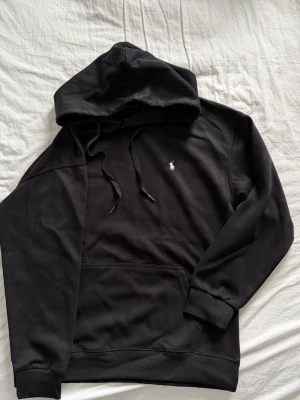 Svart hoodie från Polo Ralph Lauren - Snygg svart hoodie från Polo Ralph Lauren med klassisk vit broderad logga på bröstet. Hoodien har huva med dragsko, storlek L men sitter som M
