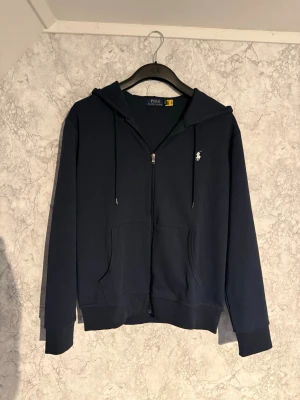 Mörkblå Ralph Lauren Zip Hoodie - Tjena, säljer nu en mycket fin mörkblå Ralph Lauren hoodie, den är använd fåtal gånger och har inga defekter. Perfekt nu inför hösten. Storlek M, har du någon fundering är de bara att skriva och ge gärna prisförslag!!