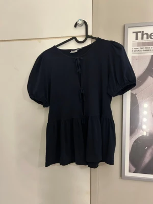 Mörkblå blus med knyt och puffärm - Supersöt mörkblå blus med puffärmar och knyt framtill. Blusen har en lös passform och volang nedtill som ger en avslappnad och trendig look. Perfekt att styla med jeans eller kjol för en cool vibe.