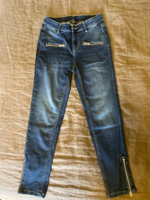 Mörkblå jeans med dragkedjor - Stl. 34(XS) mörkblå jeans med  dragkedjor vid benslut och framtill vid fickorna. Från Kappahl 