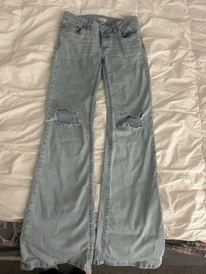 Ljusblå bootcut jeans - Säljer ett par lågmidjade ljusblå bootcut jeans med slitna hål på båda knäna och coola detaljer på bakfickan💞