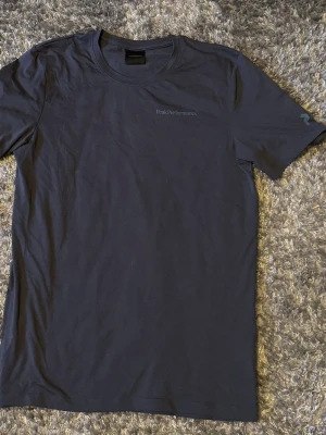 Mörkblå t-shirt från Peak Performance - Snygg mörkblå t-shirt från Peak Performance med diskret logga på bröstet. Klassisk rund halsringning och korta ärmar. Tillverkad i mjuk bomull som känns skön mot huden. Perfekt till jeans eller shorts för en clean look.