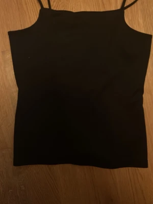 Svart linnetopp med smala axelband Pris kan diskuteras! - En enkel och stilren svart linnetopp med smala axelband. Toppen har rak passform och ärmlös design, perfekt att matcha med jeans eller kjol. Materialet känns mjukt och följsamt mot huden.