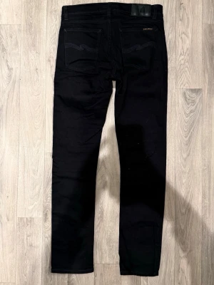 Nudie Jeans Grim Tim Svarta W31/L32 - Slim Straight Fit - Nudie Jeans Grim Tim svarta jeans med slim straight fit-passform, normal midja och raka ben, storlek W31/L32, midja 39 cm, ytterbenslängd 104 cm, benöppning 16 cm, modellen är 185cm & väger 65kg, i fint skick.