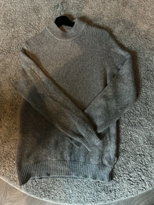  stickad tröja från NN07 - Säljer en stilren grå stickad tröja från NN07 med  krage och ribbade muddar. Tillverkad av italienskt garn för extra mjuk och lyxig känsla. Perfekt till höstens och vinterns outfits.