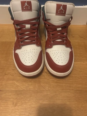 Air Jordan 1 High röd och vit - Snygga Air Jordan 1 High sneakers i rött och vitt med klassisk Jumpman-logga på plösen. Skorna har högt skaft, perforerad tåbox och röda snören. Tillverkade i läder. Knappt använda bara 3 gånger ungefär då jag växte ur dem.