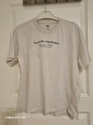 Vit t-shirt från 157 med tryck - Vit t-shirt från 157 med svart texttryck 'Nouvelle Aquitaine' på bröstet. Klassisk rund halsringning och korta ärmar. Tillverkad i 100% bomull för en mjuk och bekväm känsla. Perfekt till jeans eller shorts för en enkel och clean look.