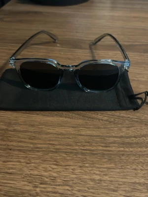 chimi liknade glasögon  - Säljer ett par stilrena solglasögon med transparent båge och svarta, fyrkantiga linser. Glasögonen har en modern och clean look som passar till de flesta outfits. Kommer med en svart tygpåse för förvaring. Uv skydd ska det vara men har inte testat att det finns uv skydd.