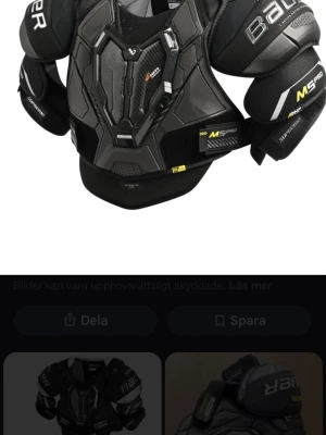 Svart axelskydd Bauer M5 Pro - Säljer ett svart axelskydd Bauer M5 Pro med robust design och extra skydd vid axlar och bröst. Skyddet har gula detaljer och är gjort i slitstarkt syntetmaterial, perfekt för intensiva sportaktiviteter som hockey.