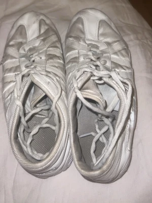 Vita NFINITY cheerleading skor - Säljer ett par vita cheerleading skor. Skorna har paneler i syntet och textil, samt en platt sula för skön komfort. Perfekt för dig som går cheerleading.