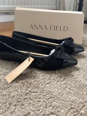 Svarta ballerinaskor med rosett Anna Field - Säljer ett par eleganta svarta ballerinaskor från Anna Field med lackfinish och rosett framtill. Endast provade och i nyskick.  Storlek 38, men jag skulle säga att de är något stora i storleken och passar bättre en 39. Säljes eftersom de är för stora för mig.