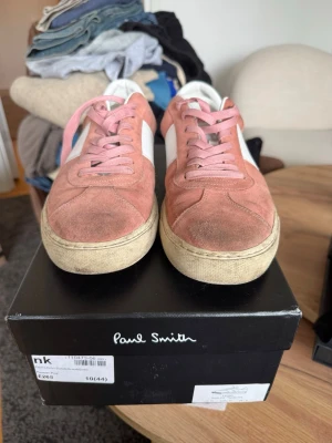 Rosa sneakers från Paul Smith - Snygga sneakers i rosa mocka med vita detaljer och rosa skosnören från Paul Smith. Skorna har en klassisk låg modell med vit sula och vit häl. Perfekta för dig som vill ha en stilren och trendig look. Nypris: 3000kr