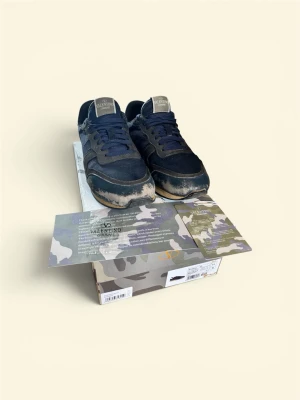 Valentino blå sneakers med camo-detaljer - Snygga sneakers från Valentino i mörkblått med camo-detaljer och beige inslag. Skorna har en klassisk låg siluett, mesh och mocka-paneler samt gummisula. Perfekta för dig som vill ha en unik touch på din streetwear. Priset ej hugget i sten