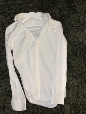 Vit skjorta från These Glory Days - Klassisk vit skjorta från These Glory Days i slim fit-modell. Skjortan har långa ärmar, knappar framtill och är tillverkad i ett mjukt bomullstyg. Perfekt för en clean och stilren look. Sitter som en Small!