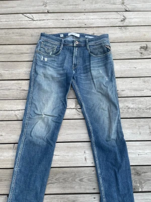 Blå raka jeans med slitningar - Säljer ett par blå jeans med raka ben och snygga slitningar framtill och baktill. Jeansen har klassisk femficksmodell, ljusare tvättade partier och detaljerade sömmar. Perfekta för en avslappnad och trendig look. Jeansen är i väldigt bra skick, ny pris 1999kr 