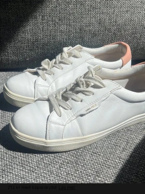 Vita sneakers med rosa/beige detalj - Snygga vita sneakers från Anna Field med klassisk låg profil och vita snören. Skorna har en ljusrosa detalj på hälen och är gjorda i slätt konstläder. Perfekta för en clean och stilren look.