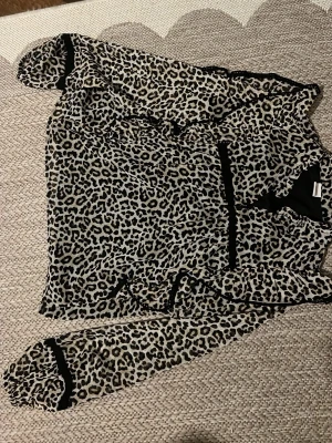 Leopardmönstrad transparent blus - Snygg leopardmönstrad blus i transparent material med svarta detaljer. Blusen har långa ärmar och volang vid axlarna. Perfekt för dig som vill sticka ut med ett trendigt djurmönster.