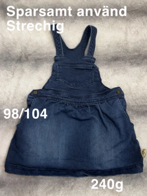 Mörkblå jeanskjol med hängslen - Säljer en mörkblå jeanskjol med hängslen och ficka framtill. Kjolen har knappar i sidorna och är gjord i stretchigt bomullsmaterial. Klassisk modell som är både bekväm och stilren.🌸Sparsamt använd. Strechigt material. Storlek 98/104