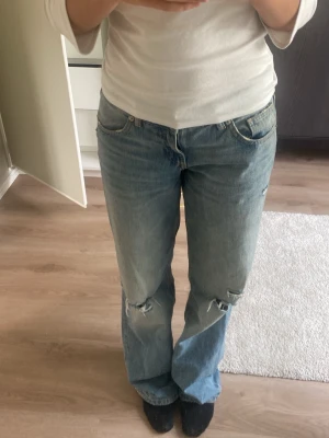 Ljusblå slitna raka jeans - Säljer ett par ljusblå jeans med raka ben och slitningar vid knäna. Jeansen har klassisk femficksmodell och normal midja. Perfekta för en avslappnad och trendig look. Materialet är denim i bomull.
